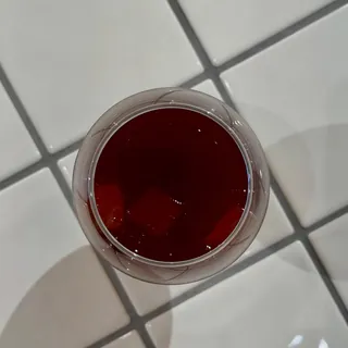 Instagram post: a glass of a red drink seen from above on white tiles