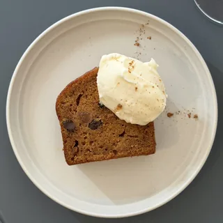 A slice of carrot cake with cream on an off-white round plate, seen from above on a blue-gray table