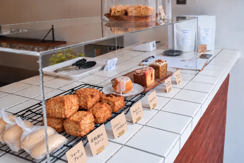 The white tiled counter with baked goods and handwritten labels behind a clear glass showcase, and bags of coffee beans toward the back