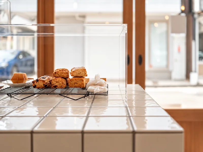 Light reflecting across the white tiled counter, with baked goods in the case and the wooden entrance beyond